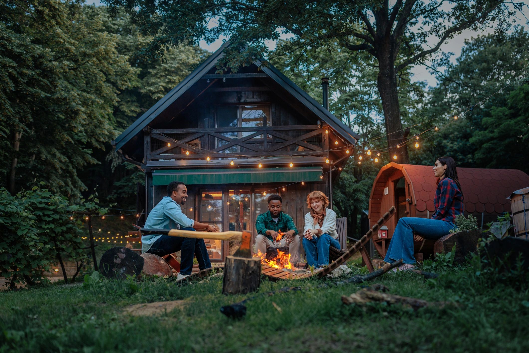 Friends gathered around a campfire near a forest cabin