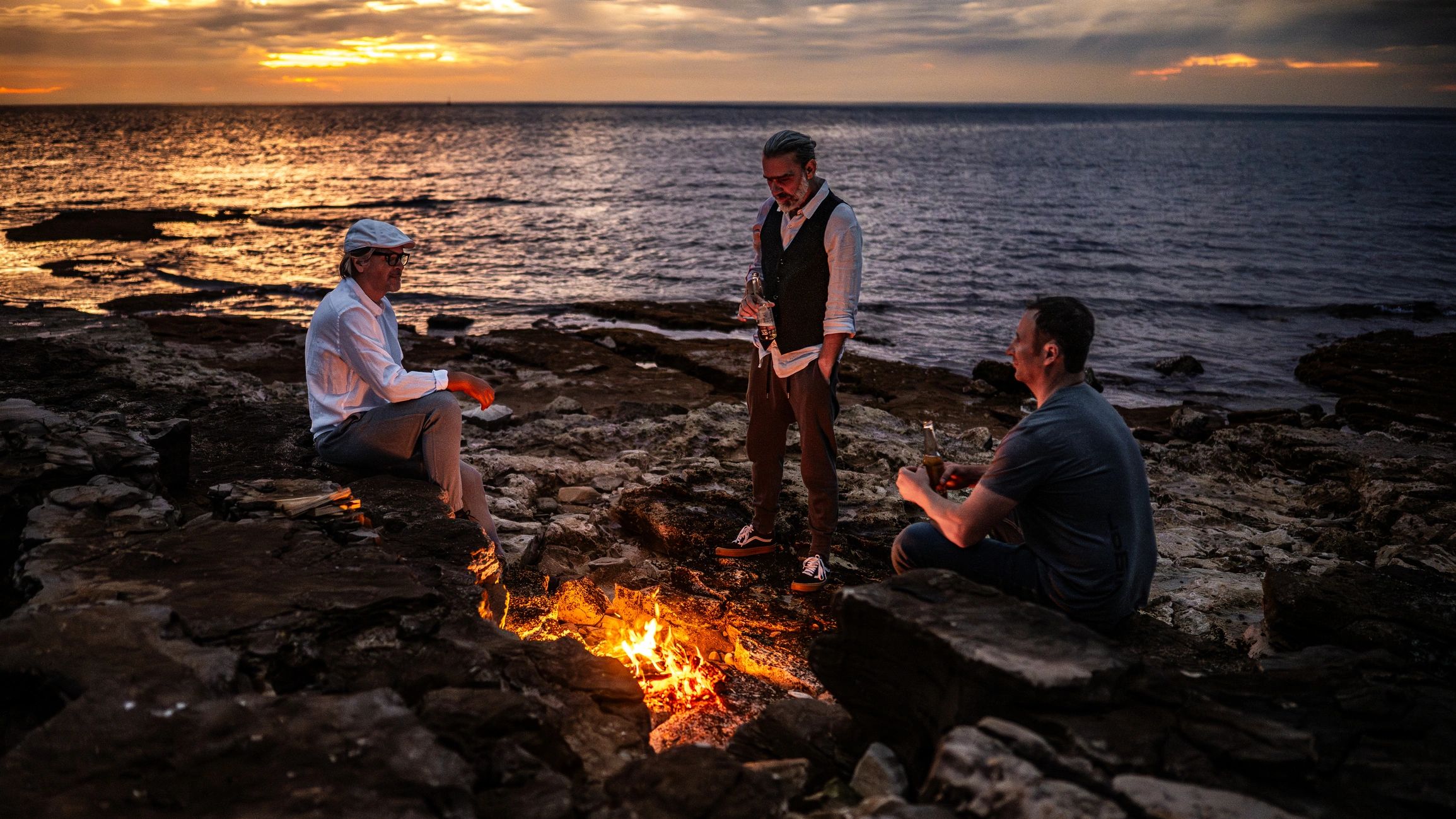 Campfire cooking scene at sunset by the water